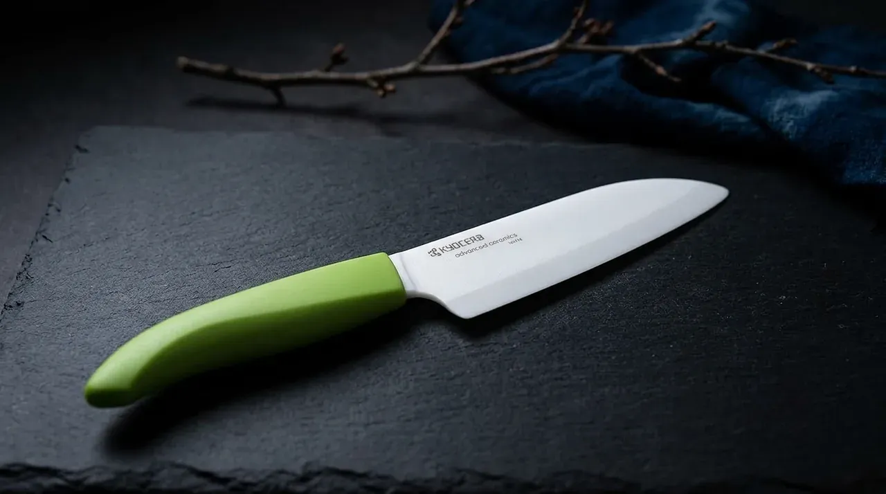 Cuchillo Kyocera Santoku de hoja blanca de cerámica y mango verde sobre pizarra oscura