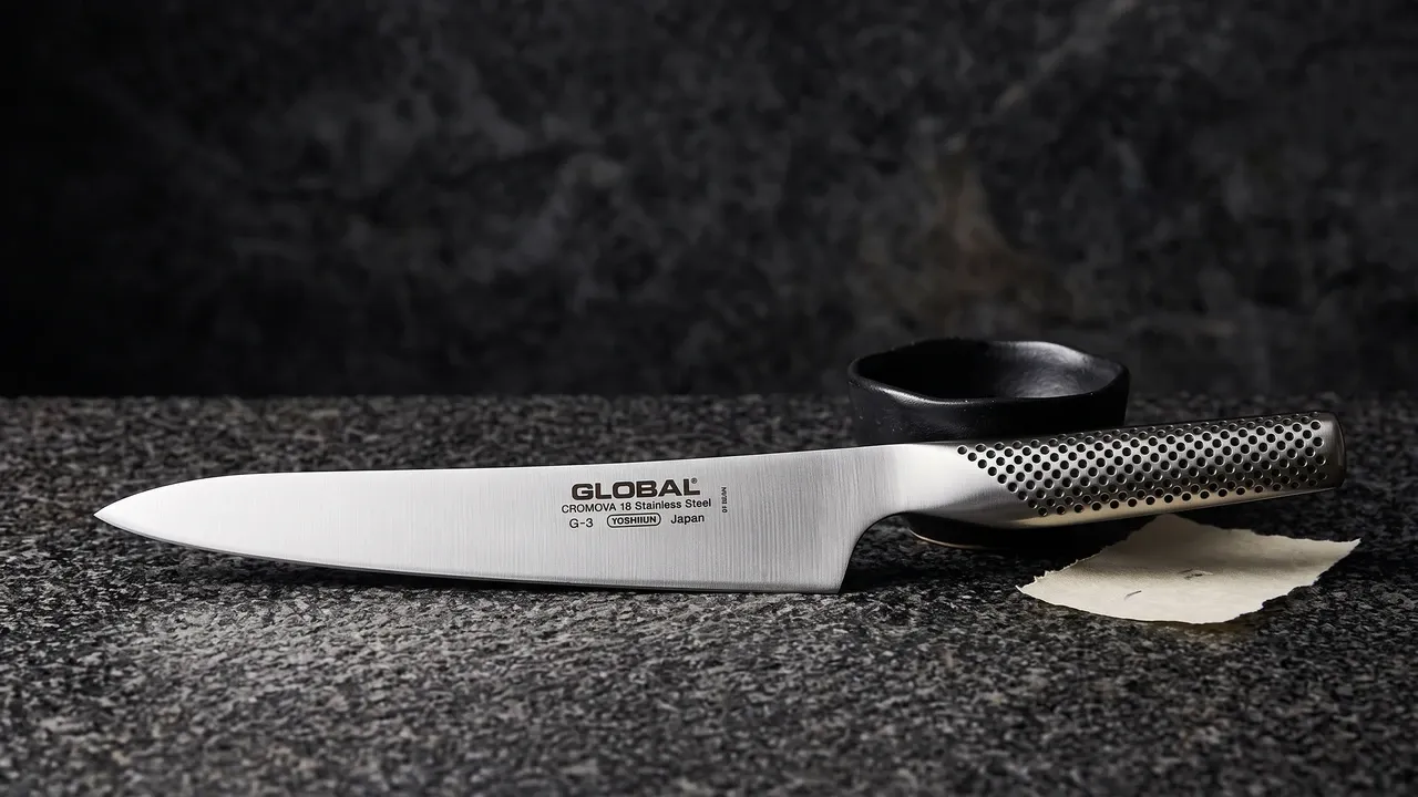 Global G-3 trinchador de 21 cm sobre granito oscuro de grano grueso, junto a un cuenco de cerámica wabi y un fragmento de papel washi