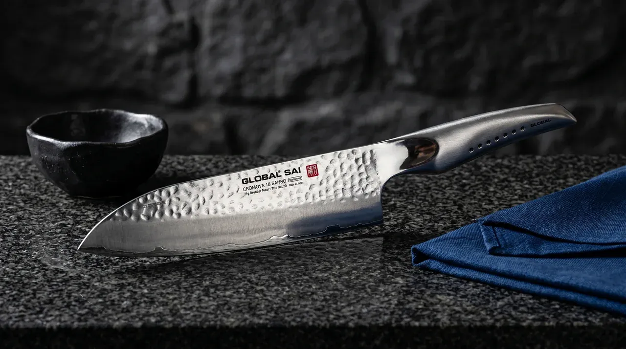 Global SAI-M03 Santoku con acabado de martillo tsuchime sobre superficie de madera oscura de Niigata