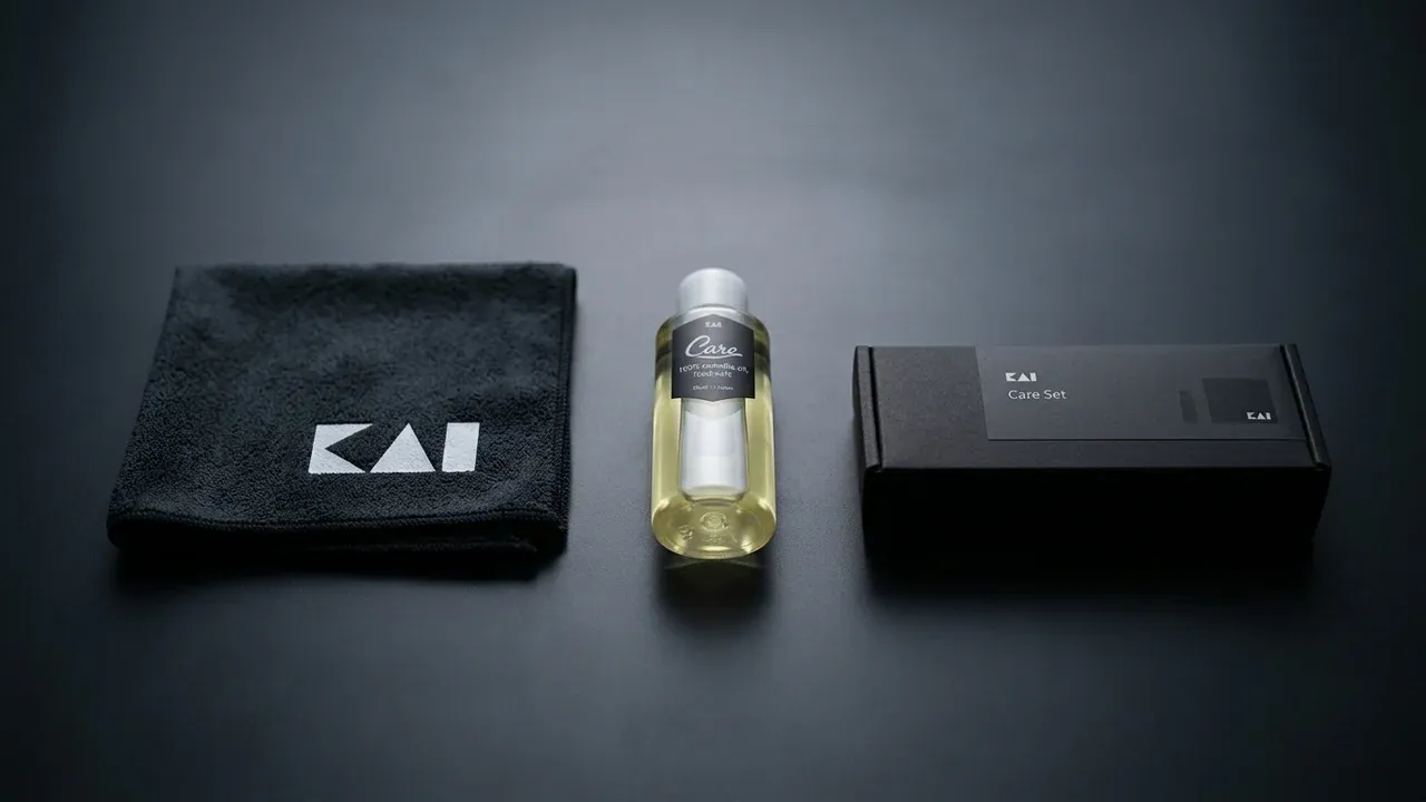 Kit completo de cuidado KAI: paño de microfibra con logo KAI, frasco de aceite de camelia Care y caja del set sobre superficie oscura