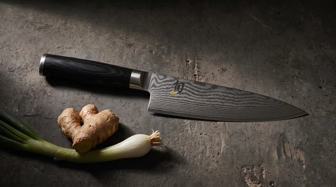 Chef KAI Shun Classic para zurdos sobre hormigón oscuro texturizado, con una raíz de jengibre y una cebolleta fresca a la izquierda