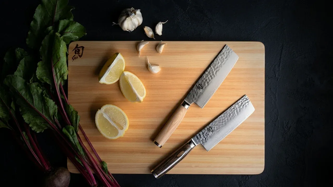 Dos cuchillos japoneses sobre la tabla de corte KAI Shun Hinoki de ciprés claro, con limones y ajo