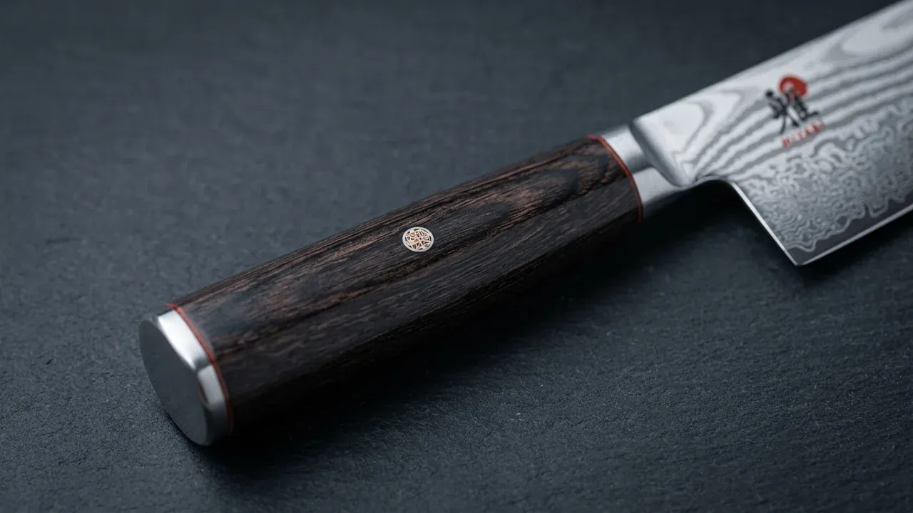 Detalle del mango octogonal de madera de abedul del santoku Miyabi 5000 FCD con el remache decorativo y el logo Miyabi