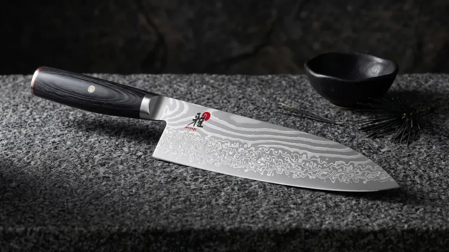 Miyabi Kaizen II Chef de 24 cm sobre granito oscuro de grano grueso, junto a un cuenco de cerámica wabi y una acícula de pino negro