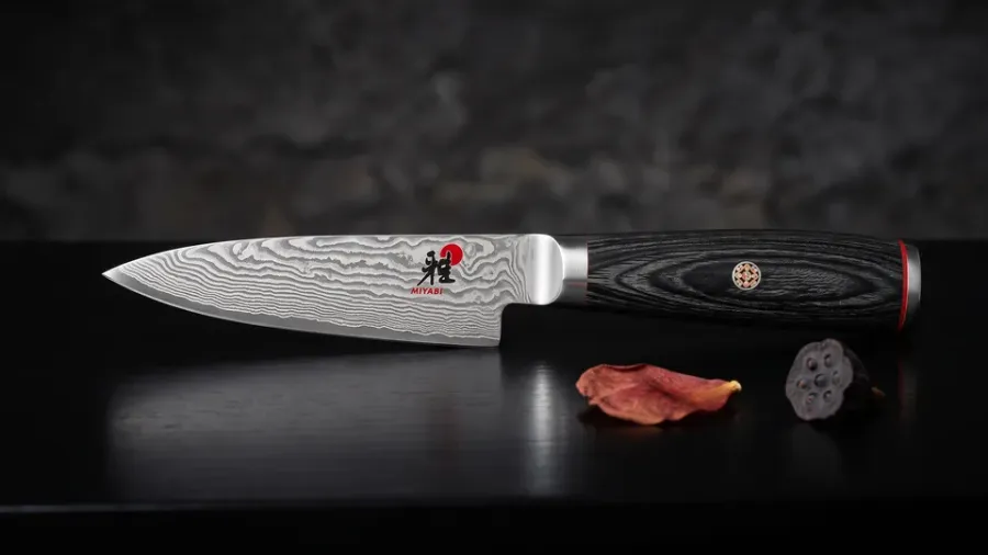 Miyabi Kaizen II Shotoh de 9 cm sobre madera lacada negra, junto a un pétalo de tsubaki seco y una semilla de loto