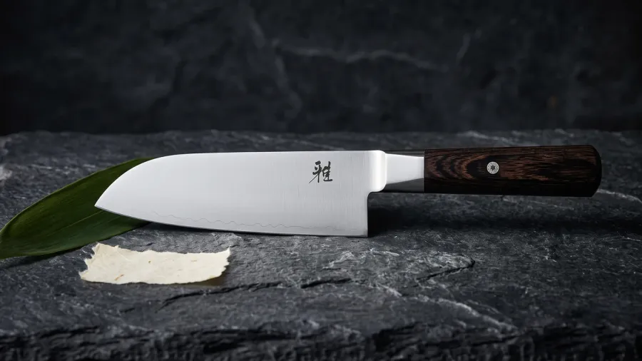 Miyabi KOH 4000FC Santoku de 18 cm sobre pizarra oscura rugosa, junto a una hoja de bambú y un fragmento de papel washi